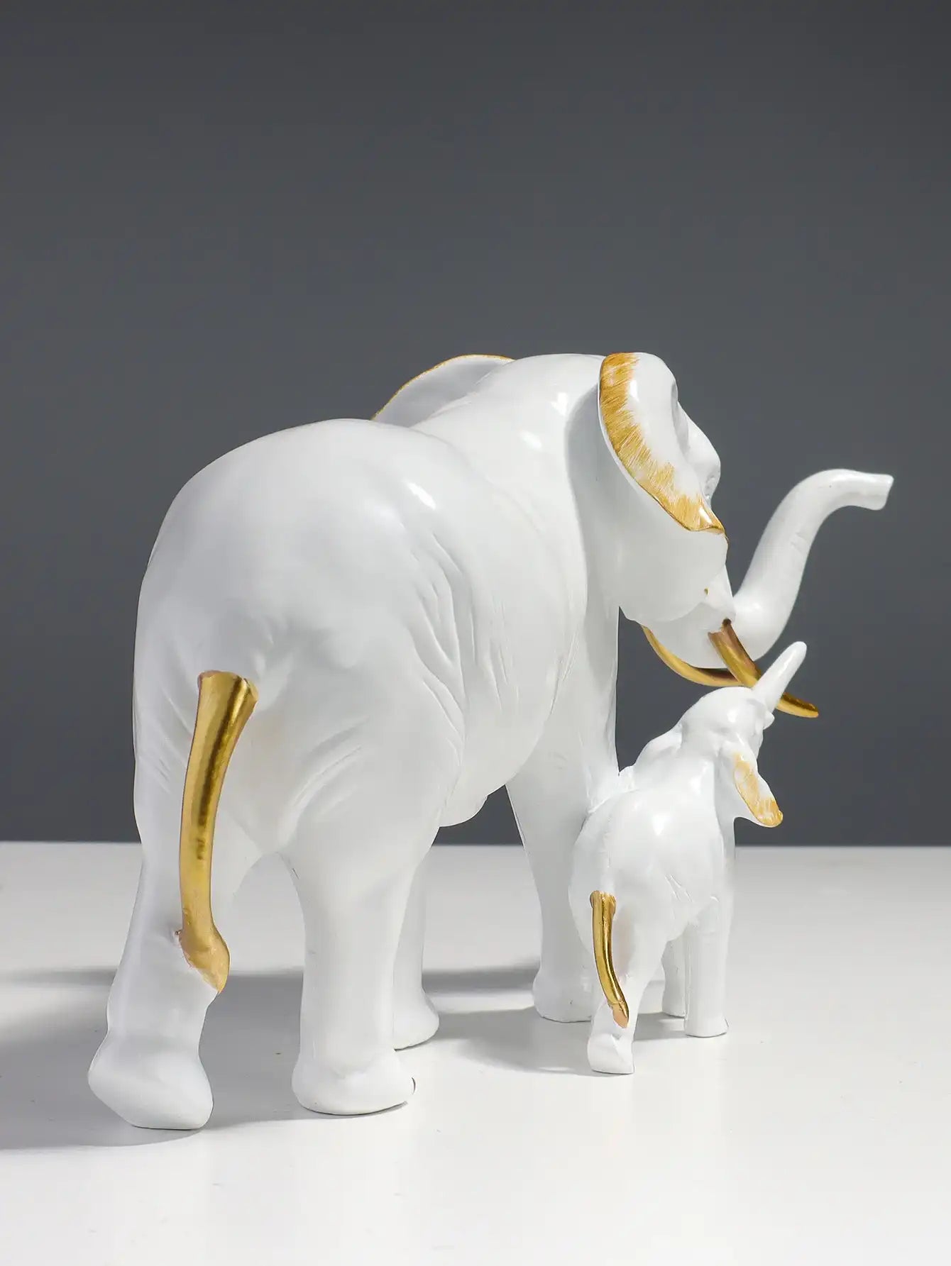 White ceramic elephant with gold accents and a smaller elephant figure on a gray background