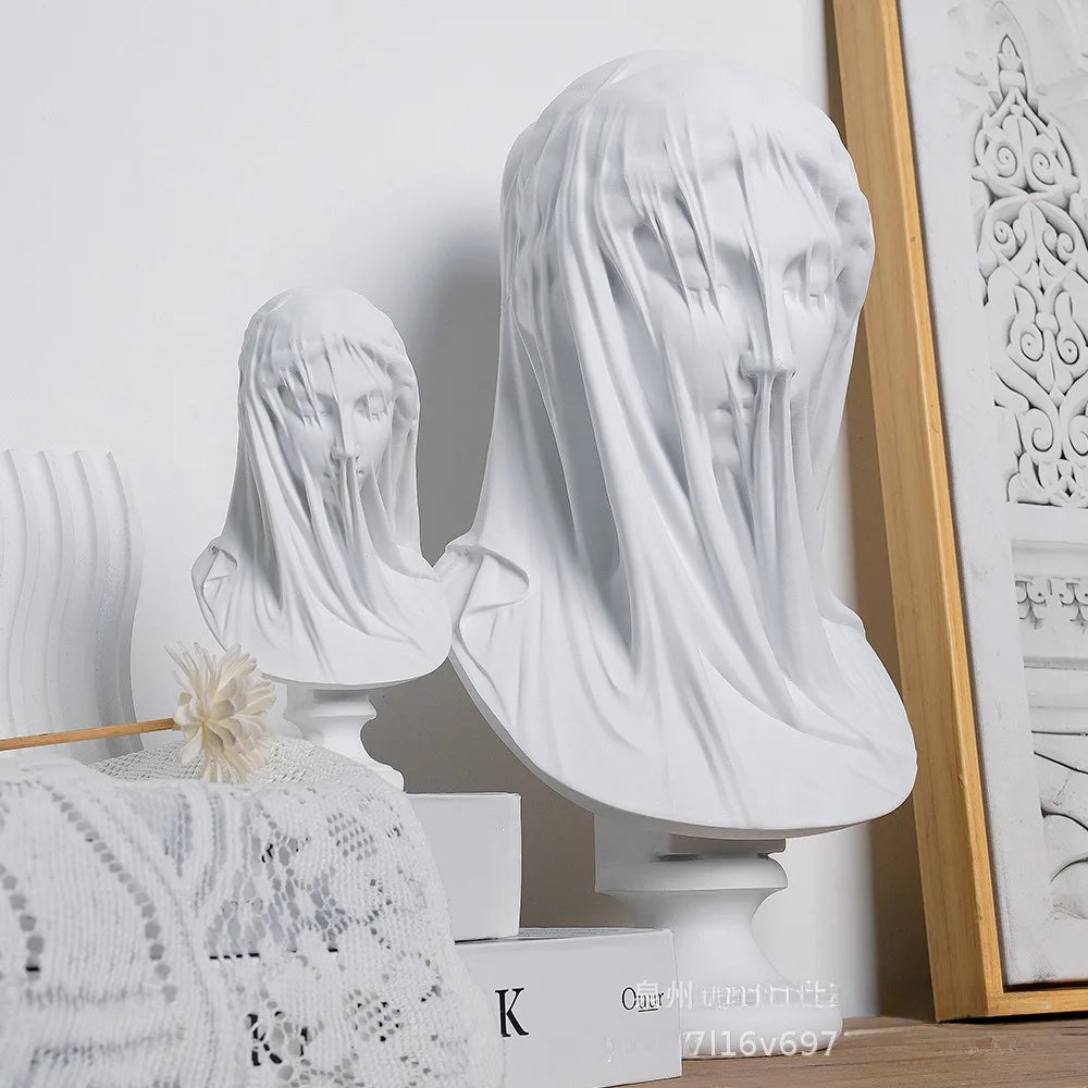 White marble busts with veils on a decorative surface with a framed picture in the background.