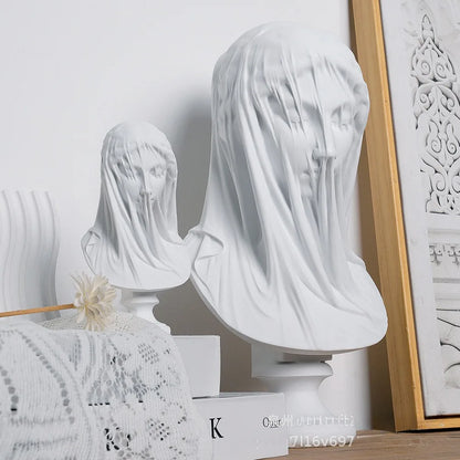 White marble busts with veils on a decorative surface with a framed picture in the background.