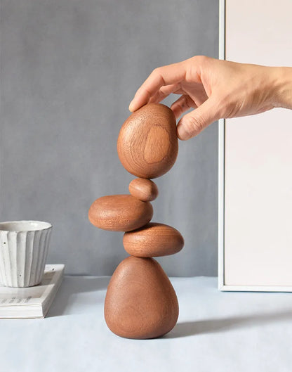 Wooden balance sculpture being adjusted by a hand on a neutral background