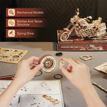 Wooden motorcycle model kit with hands assembling parts on a table.