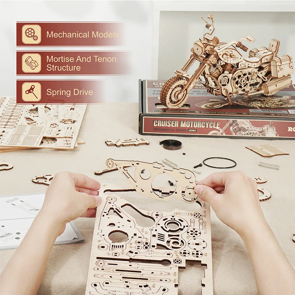 Wooden motorcycle model kit with hands assembling parts on a table.