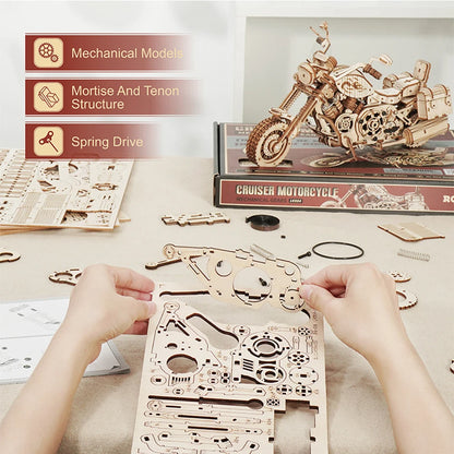 Wooden motorcycle model kit with hands assembling parts on a table.
