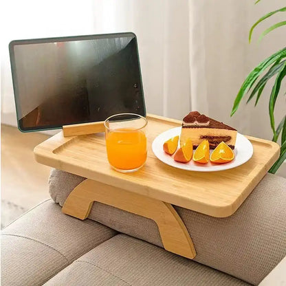 Wooden tray on a couch with a glass of orange juice and a piece of cake.