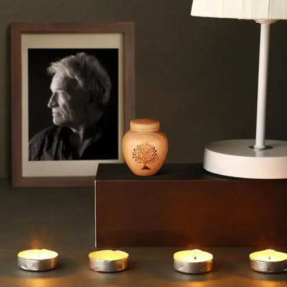 Wooden urn with a tree design on a dark surface with candles and a framed portrait.