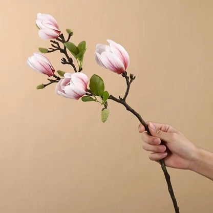 Hand holding a branch with pink flowers against a beige background