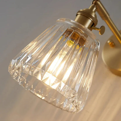 Close-up of a gold wall-mounted lamp with a clear glass shade on a neutral background