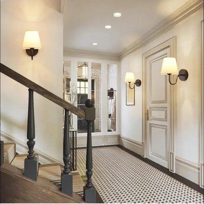 Staircase with a wall-mounted lamp with a white shade, with white walls and a patterned floor.