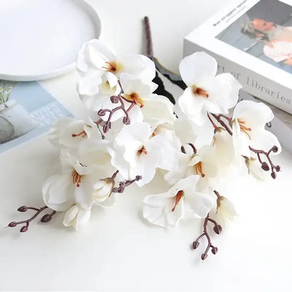 White artificial orchid flowers on a white surface with books in the background