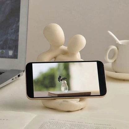 Phone stand with a phone displaying a scenic image on a desk with a laptop and teacup in the background.