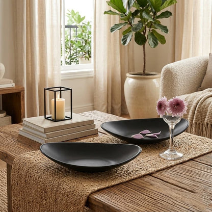 Decorative setting on a wooden table with black bowls, candles, and flowers in a living room.