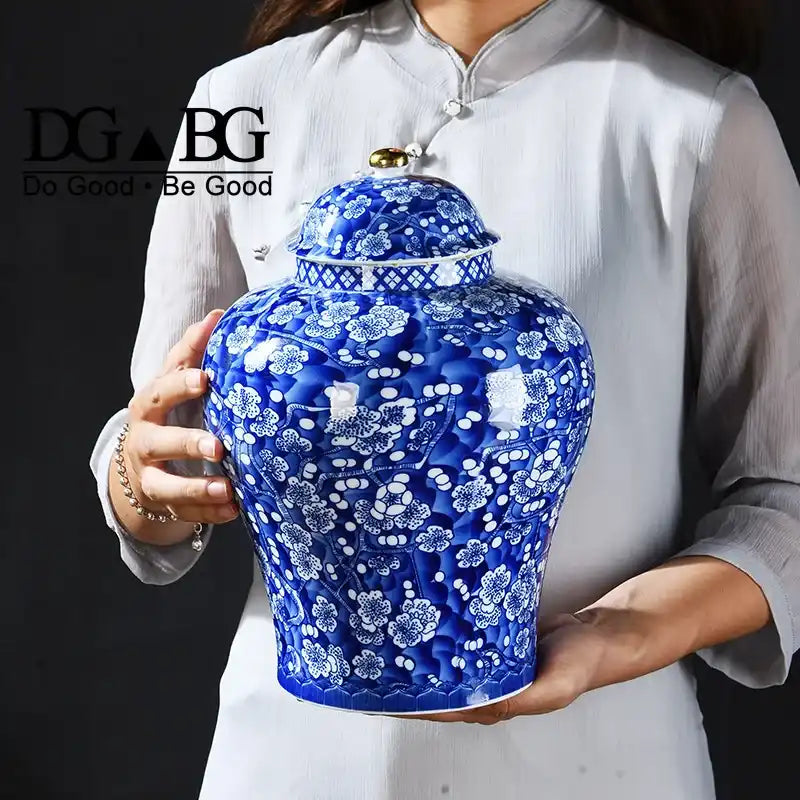 Person holding a blue ceramic vase with white floral patterns, featuring the 'DG Be Good' logo.
