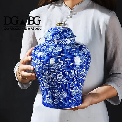 Person holding a blue ceramic vase with white floral patterns, featuring the 'DG Be Good' logo.