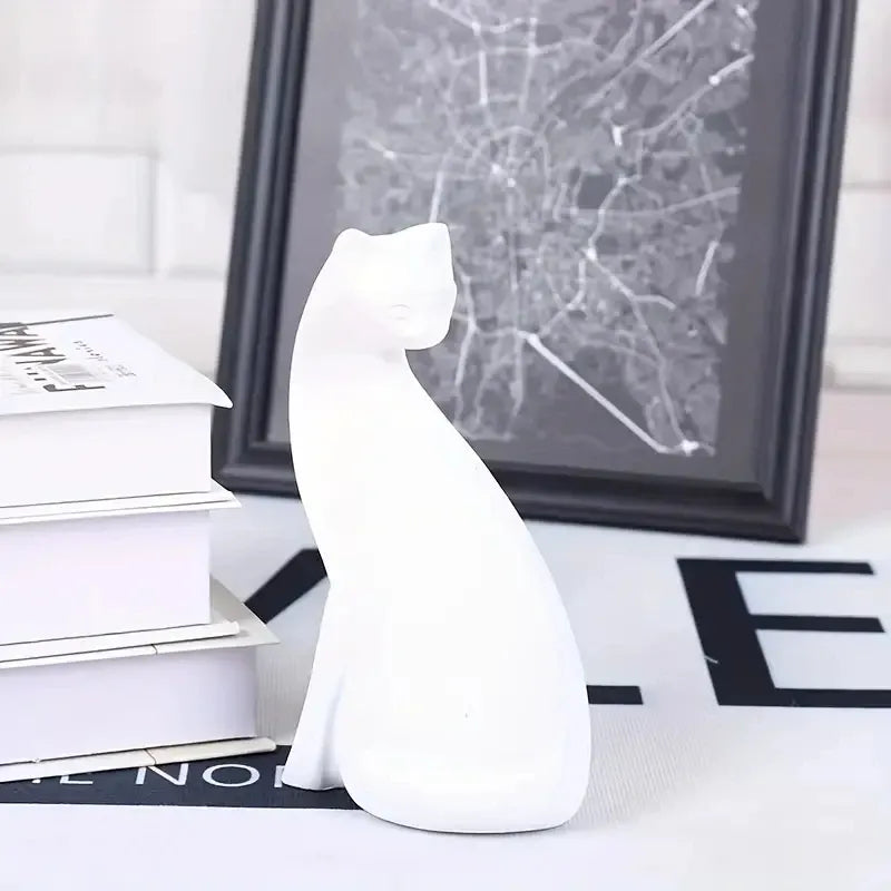 White ceramic cat figurine on a surface with books and a framed picture in the background