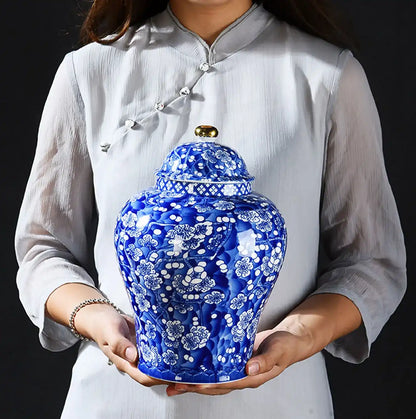 Person holding a blue ceramic jar with white floral patterns against a black background