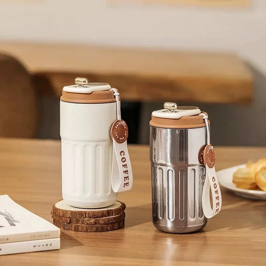 Two insulated coffee cups with wooden lids on a wooden table.