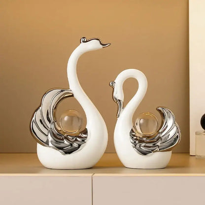 Two decorative swan figurines with silver and glass accents on a beige shelf.
