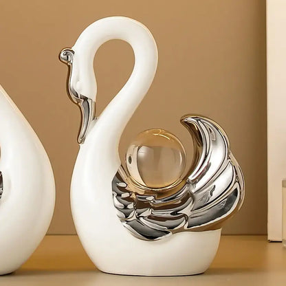 decorative swan figurines with silver and glass accents on a beige shelf.