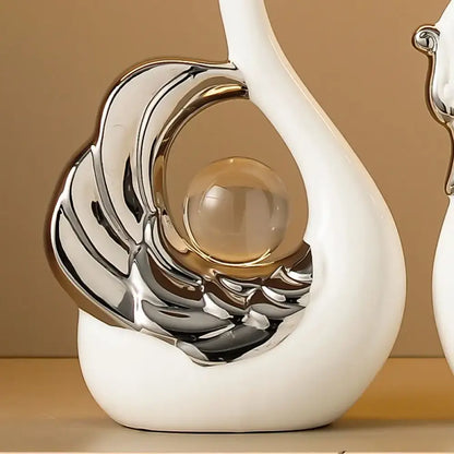 Two decorative swan figurines with silver and glass accents on a beige shelf.
