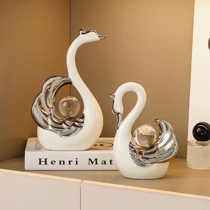 Two decorative swan figurines with silver and glass accents on a beige shelf.