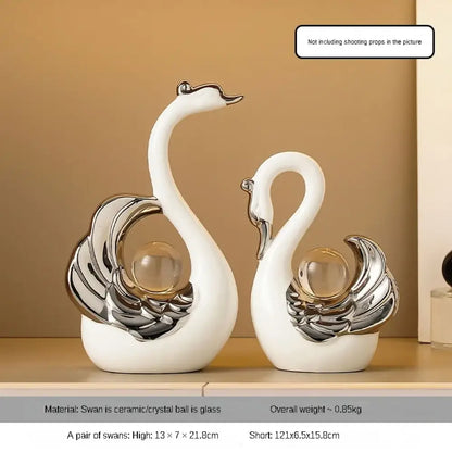 Two decorative swan figurines with silver and glass accents on a beige shelf.