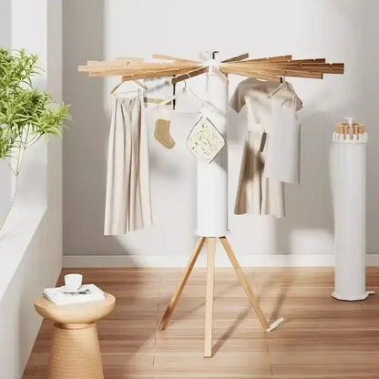 Wooden drying rack with clothes on a wooden floor in a room with a plant and white wall.