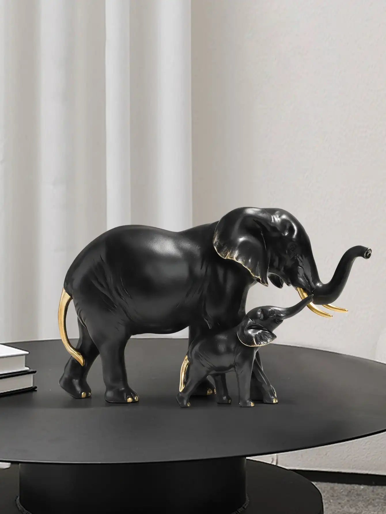 Black elephant figurine with a smaller one on a dark surface against a neutral background