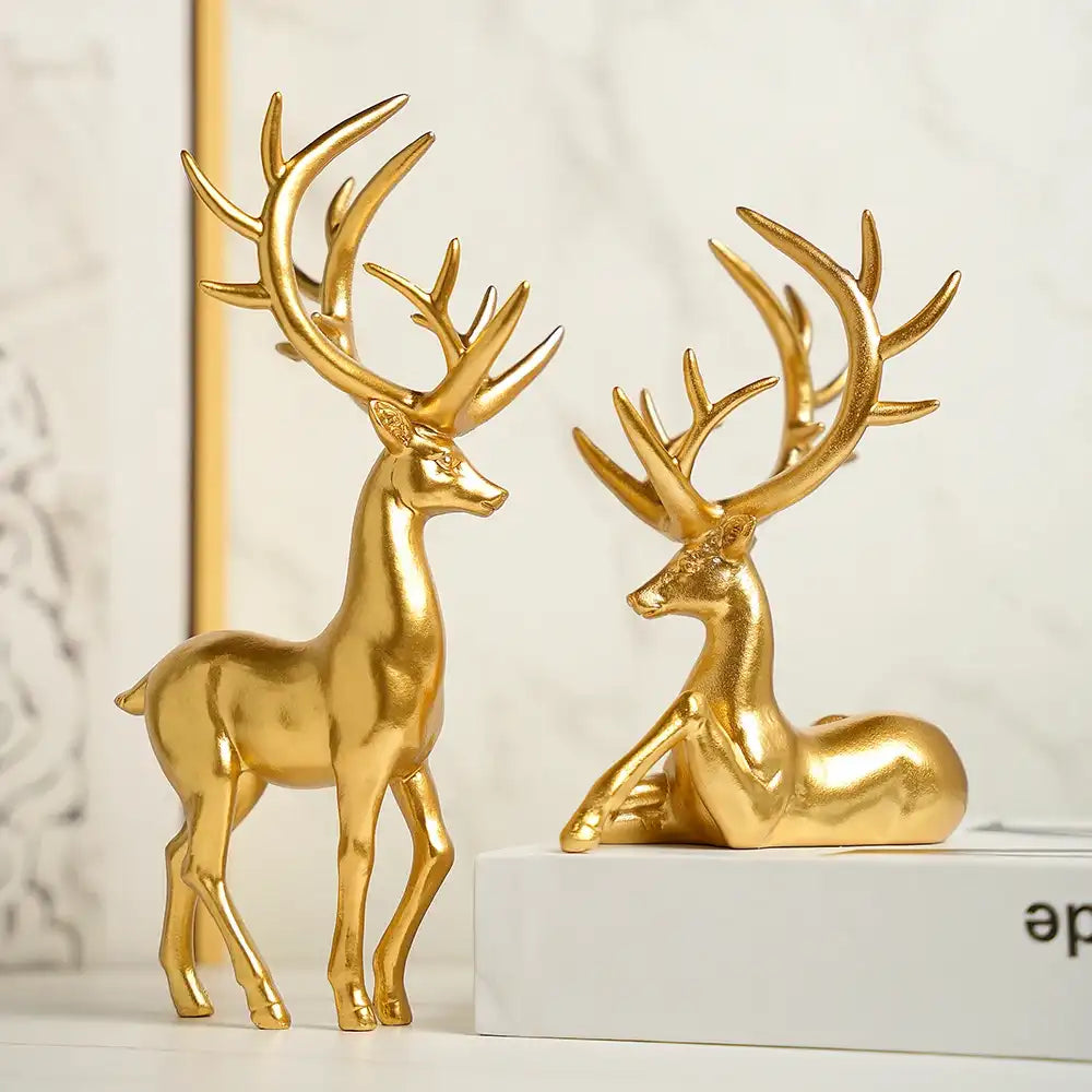 Two gold deer figurines on a white surface with a light background