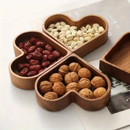 Wooden heart-shaped compartmentalized dish with nuts and dried fruits on a white surface
