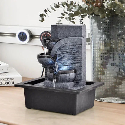 indoor fountain on a table with books and a plant in the background