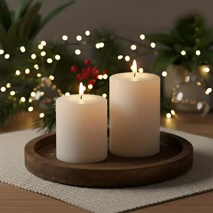 Two lit candles on a wooden tray with festive lights and decorations in the background.