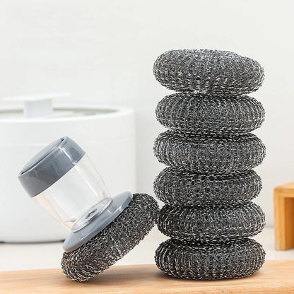 Stack of metal scrubber pads on a wooden surface with a white container in the background.