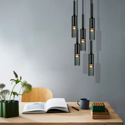 Modern office setup with pendant lights, desk, book, mug, and plants.