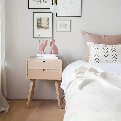 Bedroom with wooden nightstand, pink cat figurines, and framed art on the wall.