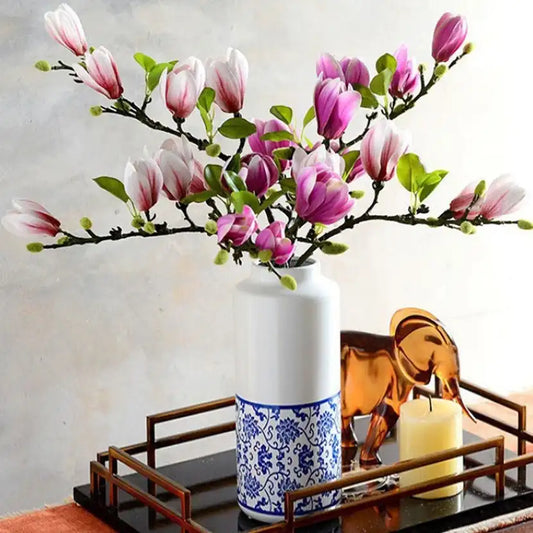 Vase with pink flowers on a decorative tray with a candle and elephant figurine.