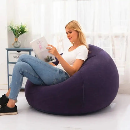 Woman sitting on a purple bean bag chair reading a book in a bright room.