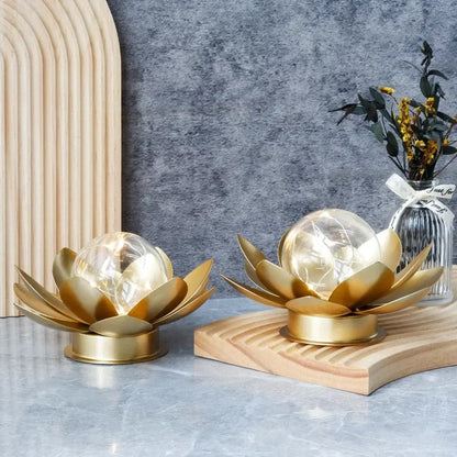 Two gold lotus-shaped lamps on a wooden stand with a gray wall and decorative elements in the background.