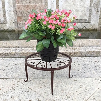 Potted plant with pink flowers on a decorative metal stand in front of stone steps.