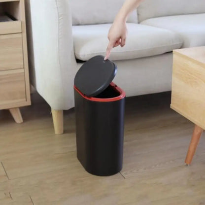 Black trash bin with a red interior and lid being opened in a living room.