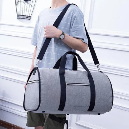 Person holding a gray duffel bag with black straps against a white wall.