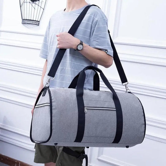 Person holding a gray duffel bag with black straps against a white wall.