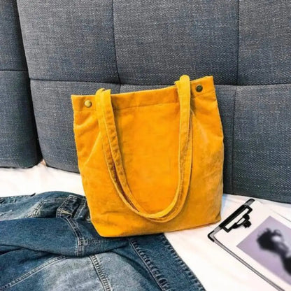 Yellow tote bag on a gray textured surface with jeans and a photo album.