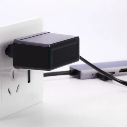 Black power adapter plugged into a wall socket with a white background