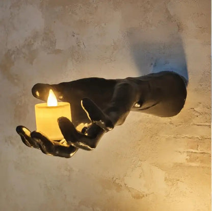 Decorative wall sculpture of a hand holding a candle against a textured wall.