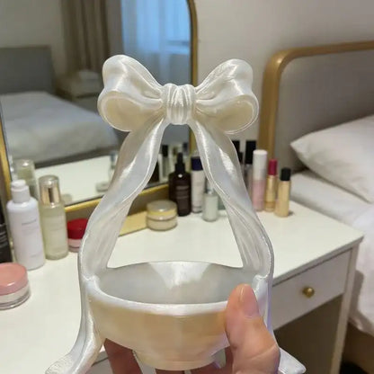 Clear face mask with a white bow held in front of a vanity mirror with skincare products.
