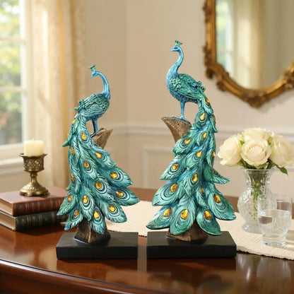 Two decorative peacock statues on a table with a mirror and flowers in the background.