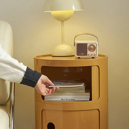 Person reaching for a book on a small wooden side table with a lamp and radio.